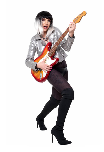Beautiful woman in sexy funky outfit and boots holding electric guitar on white background - 写真・画像