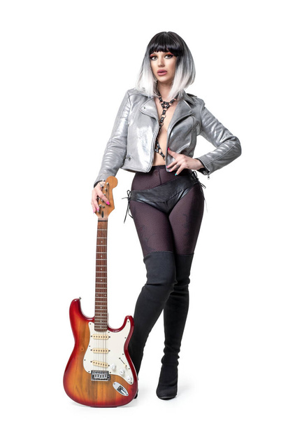 Mooie vrouw in sexy funky outfit en laarzen met elektrische gitaar op witte achtergrond - Foto, afbeelding