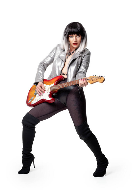 Hermosa mujer en traje funky sexy y botas sosteniendo la guitarra eléctrica sobre fondo blanco - Foto, imagen