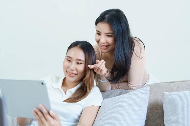 lgbtq, концепція lgbt, гомосексуальність, портрет двох азіатських жінок, які позують щасливими разом і люблять один одного, граючи планшет на дивані
. - Фото, зображення