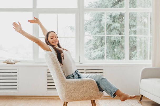 Weekend concept. A young caucasian girl sits in a chair opposite the window and pulls her hands up. Recreation, leisure lifestyle. Enjoying Morning - Foto, Imagem