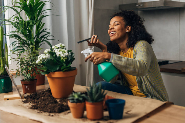 A beautiful happy woman is taking care of her plants while talking on the phone - Фото, изображение