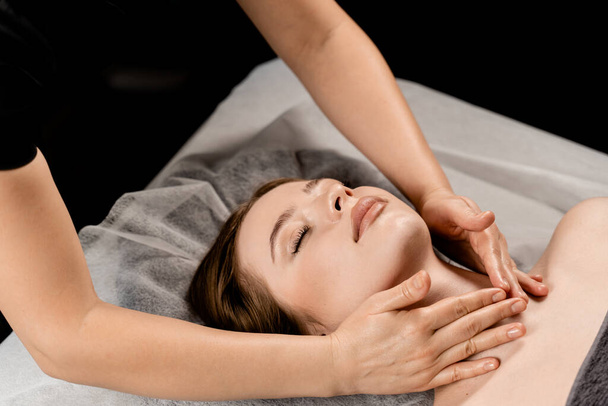 Дівчина з закритими очима розслаблює масаж обличчя та шиї у спа. Массер масаж для молодої жінки в спа-салоні. Перебудова та розслаблення - Фото, зображення