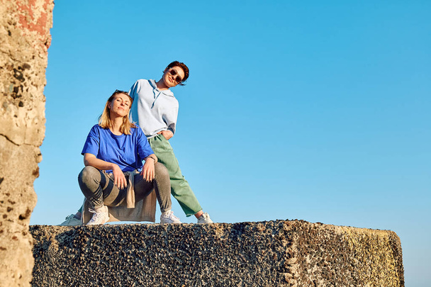 Dos novias jóvenes bailando, divirtiéndose y engañando en piedra grande en la playa con fondo azul del cielo. - Foto, imagen
