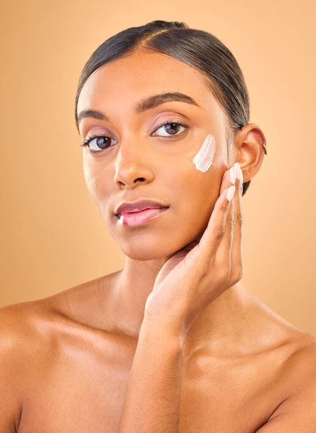 Face portrait, skincare and woman with cream in studio isolated on a brown background. Dermatology, cosmetics or confident Indian female model with lotion, beauty creme or moisturizer for skin health. - Valokuva, kuva