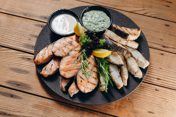 There is a new dish with sauce and cream in front of the person in the restaurant. It looks very steamy and delicious. We can see a lot slices of fish and a slice of lemon on the plate. - Foto, imagen