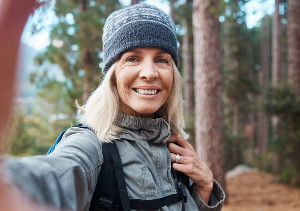 Selfie, wandelen en een oudere vrouw in het bos voor fitness, avontuur of het verkennen van de natuur. Portret, reizen en sporten met een volwassen vrouwelijke wandelaar in de bergen of bossen voor een wandeling. - Foto, afbeelding