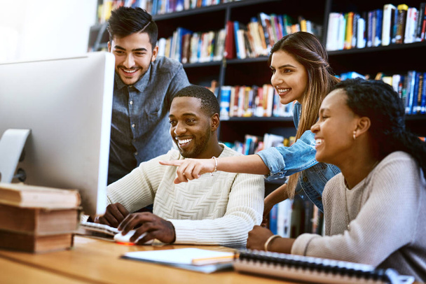 Educación en acción. un grupo de jóvenes estudiantes que usan una computadora juntos en una biblioteca universitaria - Foto, Imagen