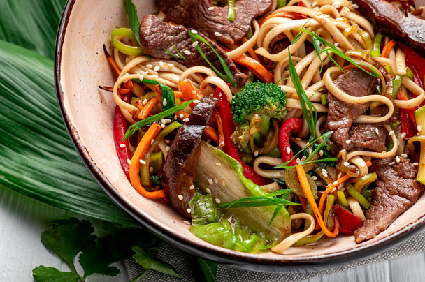Udon stir fry noodles with beef meat and vegetables in a plate on white wooden background. Asian cuisine. Delicious and healthy food. Photo for the menu. - Photo, Image