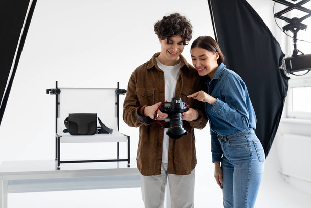 Team van professionele fotograaf en zijn vrouwelijke assistent controleren de foto 's op fotocamera tijdens het doen van content fotoshoot voor moderne tassen - Foto, afbeelding