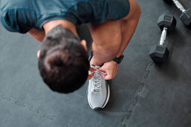 Top view, man and tie shoes in gym to start workout, training or exercise for sports. Athlete, male and tying laces on sneakers to prepare for running, cardio or exercising for health or fitness - 写真・画像
