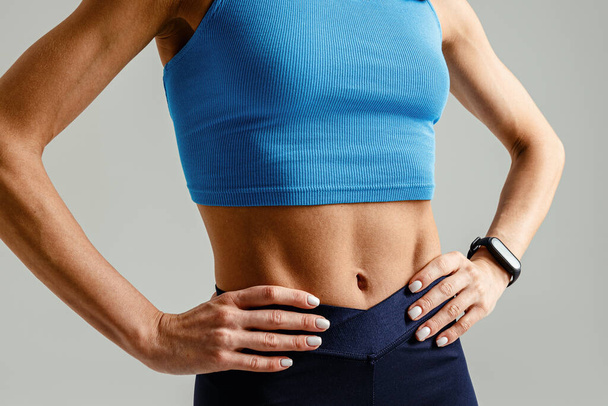 Крупный план спортивного сильного женского тела в спортивной одежде на фоне студии. Высокое качество фото - Фото, изображение