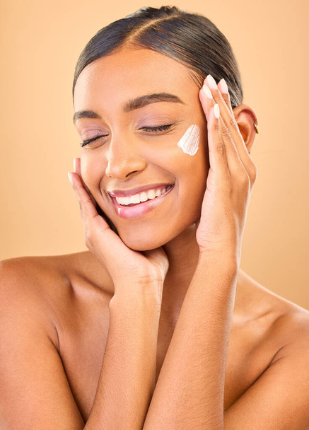 Face, skincare smile and woman with cream in studio isolated on a brown background. Dermatology cosmetics, eyes closed and happy Indian female model with lotion, creme or moisturizer for skin health - Φωτογραφία, εικόνα