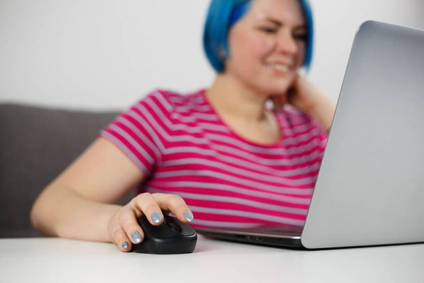 Young woman clicking with wireless mouse while working on computer at home. Freelancer person doing distant work online - Foto, afbeelding