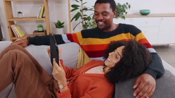 Black couple, tablet and relax on couch in home living room with comic smile, chat and social media video. Man, woman and touch screen for lying, love bond and funny meme on web, app ux and internet. - Video, Çekim