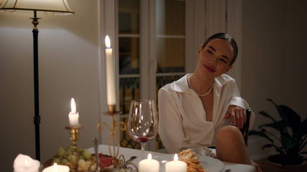 Χαμογελαστή κυρία φλερτάρει σε ρομαντικό δείπνο κοντά. Κομψό coquet γυναίκα στο βράδυ ημερομηνία διαμέρισμα. Δελεαστικό κορίτσι επικοινωνεί με άγνωστο φίλο απολαμβάνοντας ζεστά κεριά φως επέτειο - Φωτογραφία, εικόνα