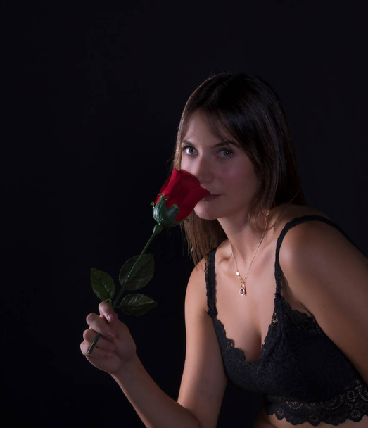 beautiful young woman in black dress holding in hand a red rose on black background - Valokuva, kuva