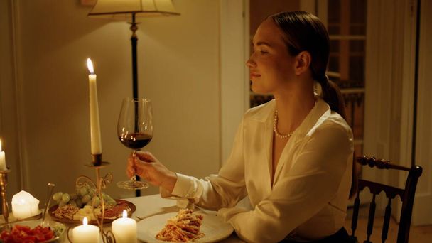 Gorgeous woman sniffing wine at candles table closeup. Seductive lady drinking grape cocktail at fancy evening dinner. Smiling girl clinking glasses tasting alcohol with unknown husband. Date concept - Photo, Image