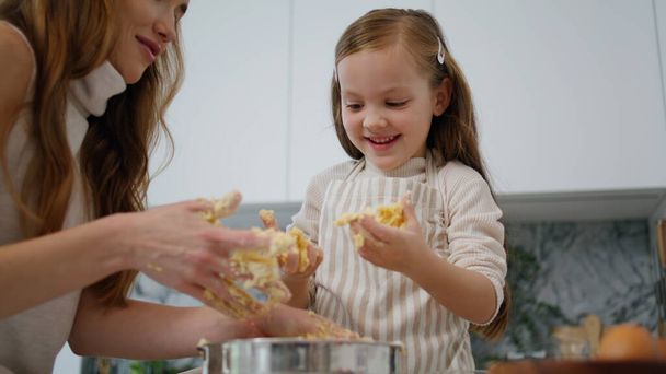 Funny baby playing dough at cook place close up. Caring mother removing pastry from kid hands at kitchen. Positive family creating cake together at home. Smiling woman spending time with daughter - Φωτογραφία, εικόνα