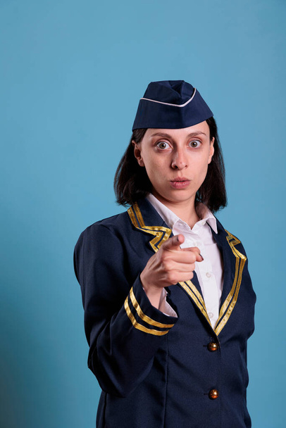 Jonge serieuze stewardess wijst naar camera met vinger, luchtvaart academie rekrutering concept. Zelfverzekerde luchtvaartmaatschappijen stewardess in professionele uniform portret vooraanzicht - Foto, afbeelding