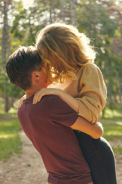 Красивый молодой человек держит свою девушку в лесу на солнце. Вертикальный открытый кадр. - Фото, изображение