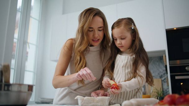 Любопытная дочь украшает торт с мамой на кухне крупным планом. Любящая женщина учит детей печь дома. Дружелюбный семейный десерт. Мать-одиночка и девочка наслаждаются домашней рутиной вместе - Фото, изображение