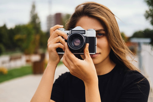 Primo piano di una bella giovane donna che scatta una foto con una fotocamera vintage all'aperto. - Foto, immagini