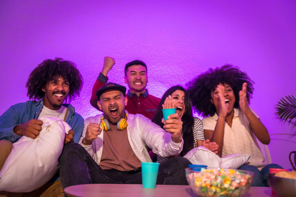 Adult party. Young people sitting on the sofa watching a football game with popcorn. Emotion for soccer, purple led, very happy celebrating a goal - Foto, immagini