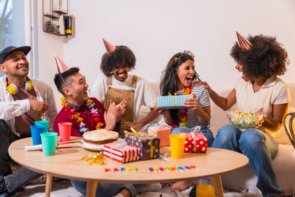 Group of friends at a birthday party on the sofa at home smiling delivering the gifts, surprising the birthday girl - 写真・画像