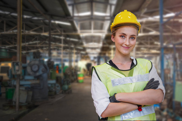 Porträt einer Arbeiterin steht selbstbewusst mit blauem Arbeitsanzug und Schutzhelm vor der Maschine und Ausrüstung für die Schwerindustrie. Stahlwerk. - Foto, Bild