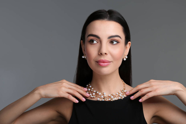 Beautiful young woman with elegant jewelry on dark grey background - Фото, изображение