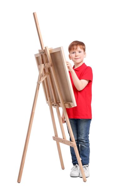 Little boy painting against white background. Using easel to hold canvas - Photo, Image