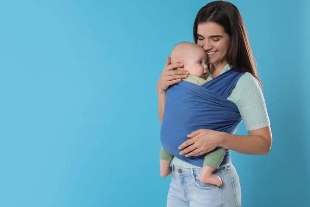 Mother holding her child in sling (baby carrier) on light blue background. Space for text - Foto, imagen
