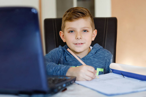 Happy healthy kid boy with glasses making school homework at home with notebook. Interested child writing essay with helping of internet. concetrated schoolchildren concept. - Φωτογραφία, εικόνα