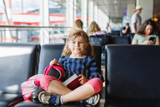 大きな窓から搭乗を待っている空港の少女。かわいい子供がパスポートを持っています家族の夏休みに出発するのを楽しみにしています. - 写真・画像