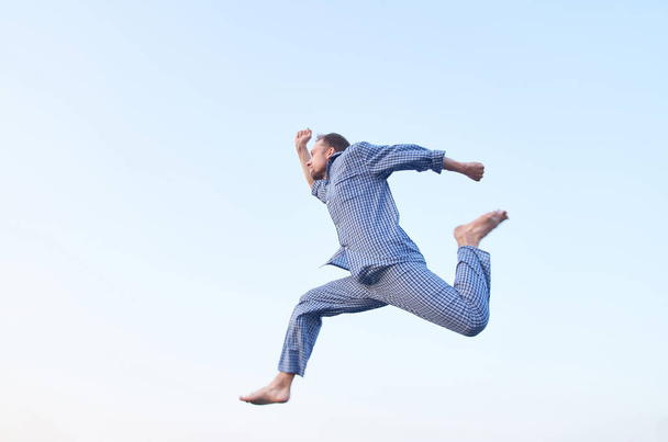 Cheerful bearded caucasian man in eyeglasses jumping in the sky outdoor in nightwear looking forward. Morning business time concept. High quality image - 写真・画像