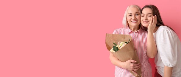 Happy young woman and her mom with flowers on pink background with space for text - Photo, Image