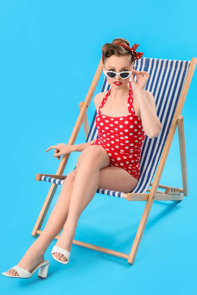 Young pin-up woman sitting in deck chair on blue background - Valokuva, kuva