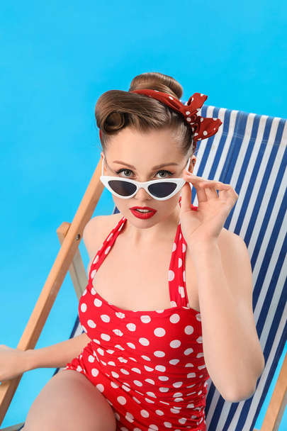 Young pin-up woman sitting in deck chair on blue background - Фото, изображение