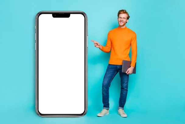 Photo of attractive cute guy dressed orange sweater eyewear pointing modern device empty space isolated turquoise color background. - Φωτογραφία, εικόνα