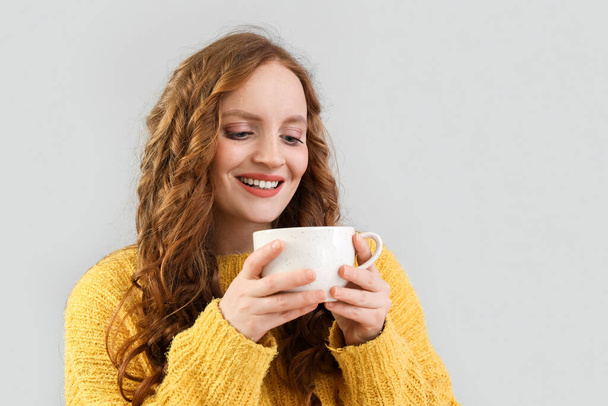 Hermosa pelirroja con taza de té sobre fondo gris - Foto, Imagen
