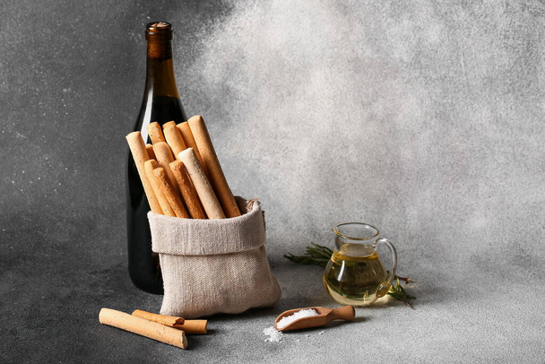 Sack bag with tasty Italian Grissini and bottle of wine on grunge background - Фото, зображення