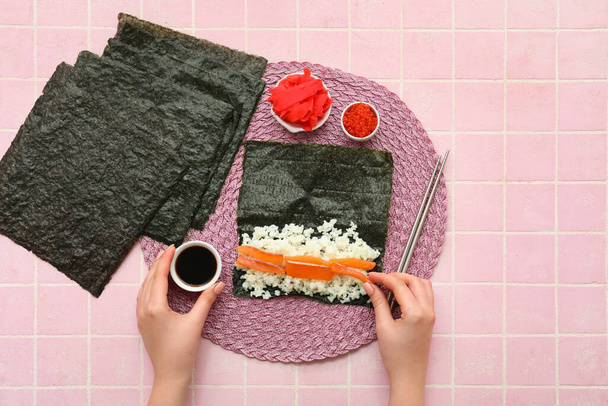 Femme préparant des rouleaux de sushi sur fond de tuiles roses - Photo, image