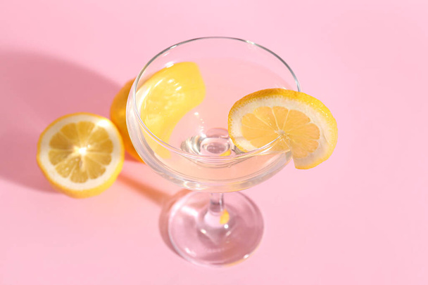 Glass of tasty martini and lemon on pink background - Фото, изображение