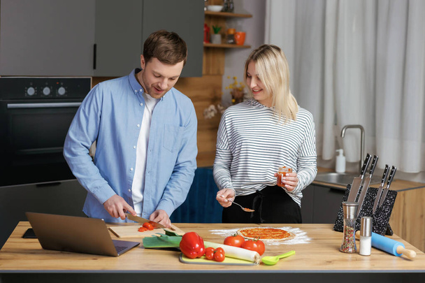 Romantic couple is cooking on kitchen. Handsome man and attractive young woman are having fun together while making salad and pizza. Healthy lifestyle concept - Foto, immagini