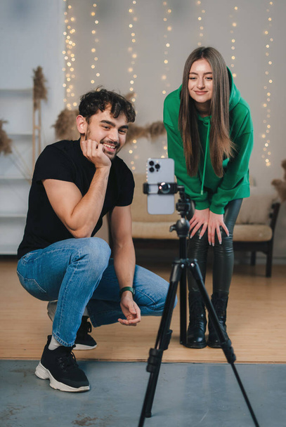 Man and woman looking at the phone that is on the stand at the video they shot to post on the internet. Successful bloggers influencers streaming video online - Фото, зображення