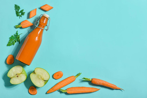 Botella de vidrio de sabroso jugo de zanahoria sobre fondo azul - Foto, imagen
