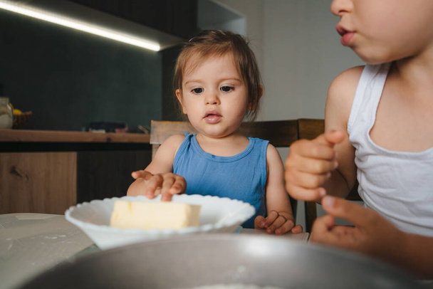 Pretty baby girl and little adorable brother sitting at table in kitchen cooking together pancakes. Family home leisure. - Photo, Image