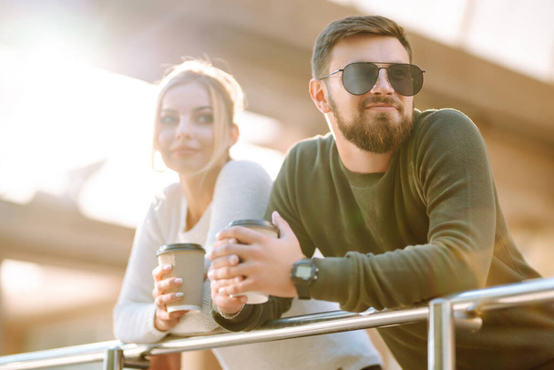 Young couple having fun talking, drinking coffee and using the phone while walking in the morning city. Relaxation, youth, love, lifestyle, selfie, blogging. - Zdjęcie, obraz