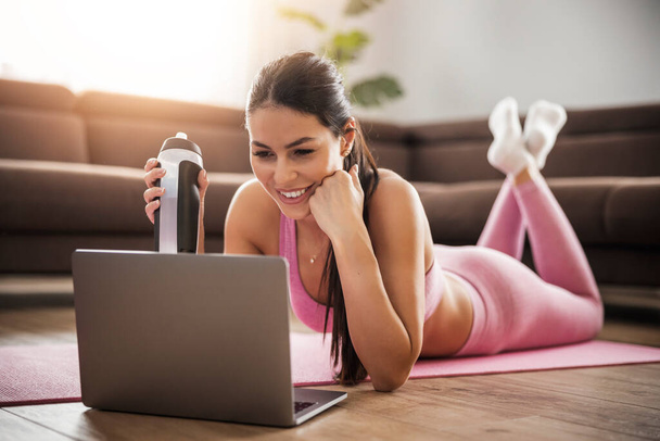Mujer de fitness en ropa deportiva haciendo ejercicio en casa delante de la computadora portátil, viendo videos de fitness. Deporte, personas y concepto de estilo de vida.. - Foto, imagen